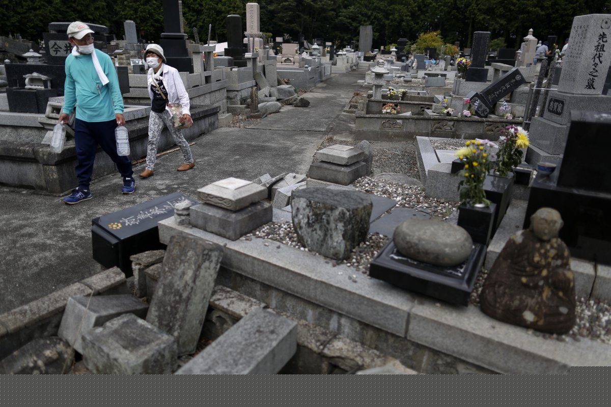 在富冈市，人们戴着口罩前往被地震破坏的墓地祭拜亲人。